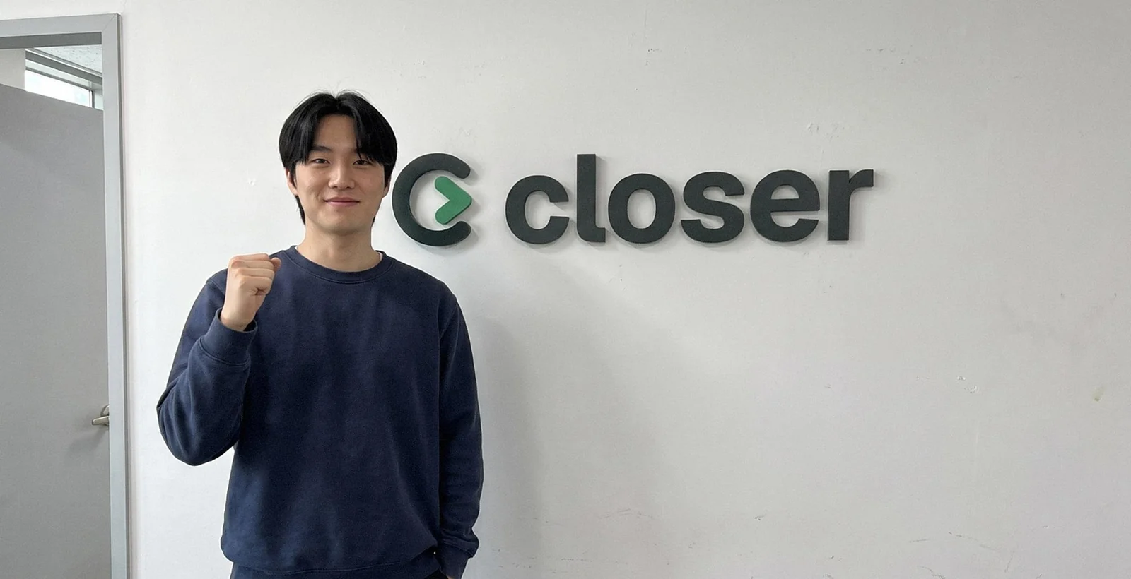 데이터 엔지니어 박준수 님이 closer 로고가 붙은 흰 벽 앞에서 주먹을 쥐고 웃는 모습